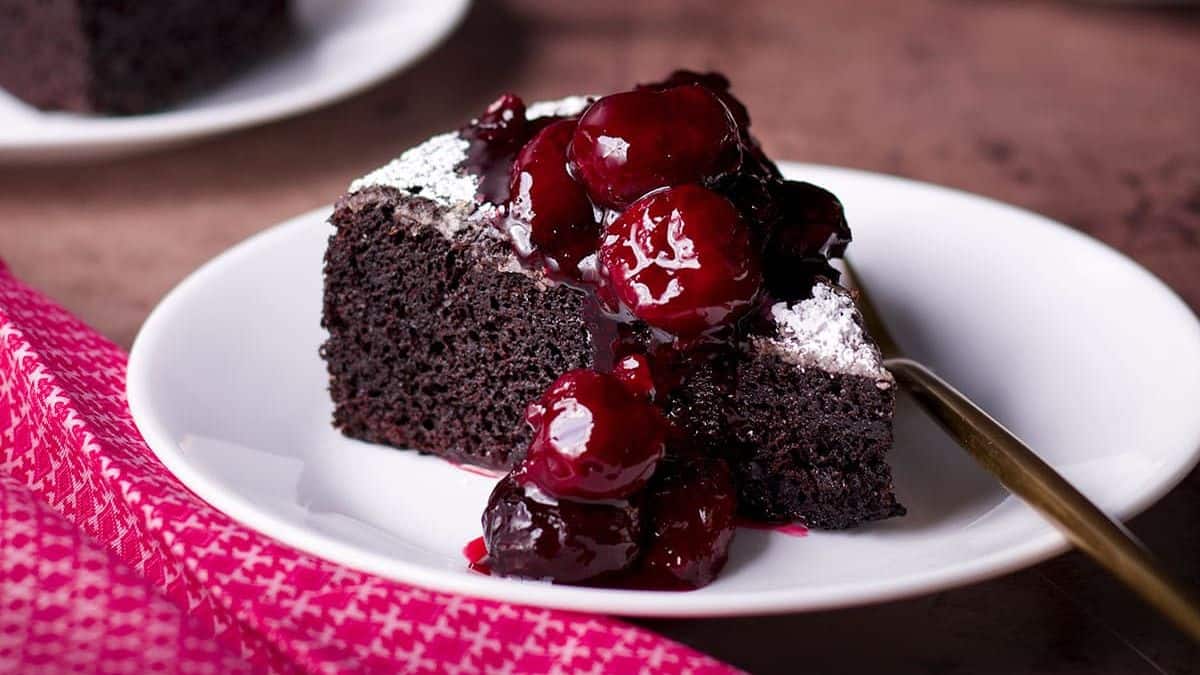 A slice of chocolate cake, dusted with powdered sugar, and then topped with berry compote.