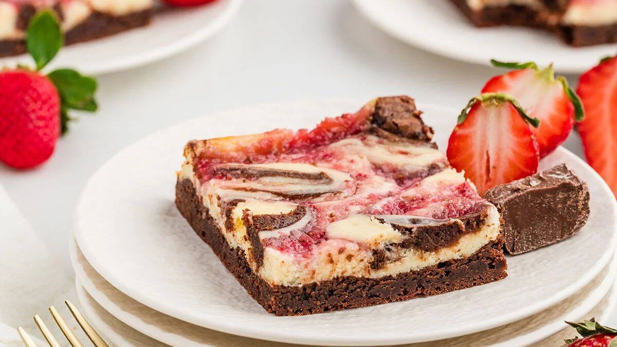 A single piece of strawberry cheesecake brownies set on a plate with strawberry slices on the side. 