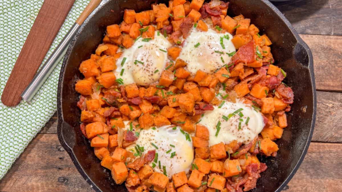Top shot of a cast iron Dutch oven filled with Sweet Potato hash a4 pieces of cooked eggs on top.