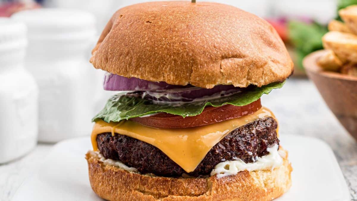Venison burger with cheese, onion, tomato, lettuce that is all set on a plate.