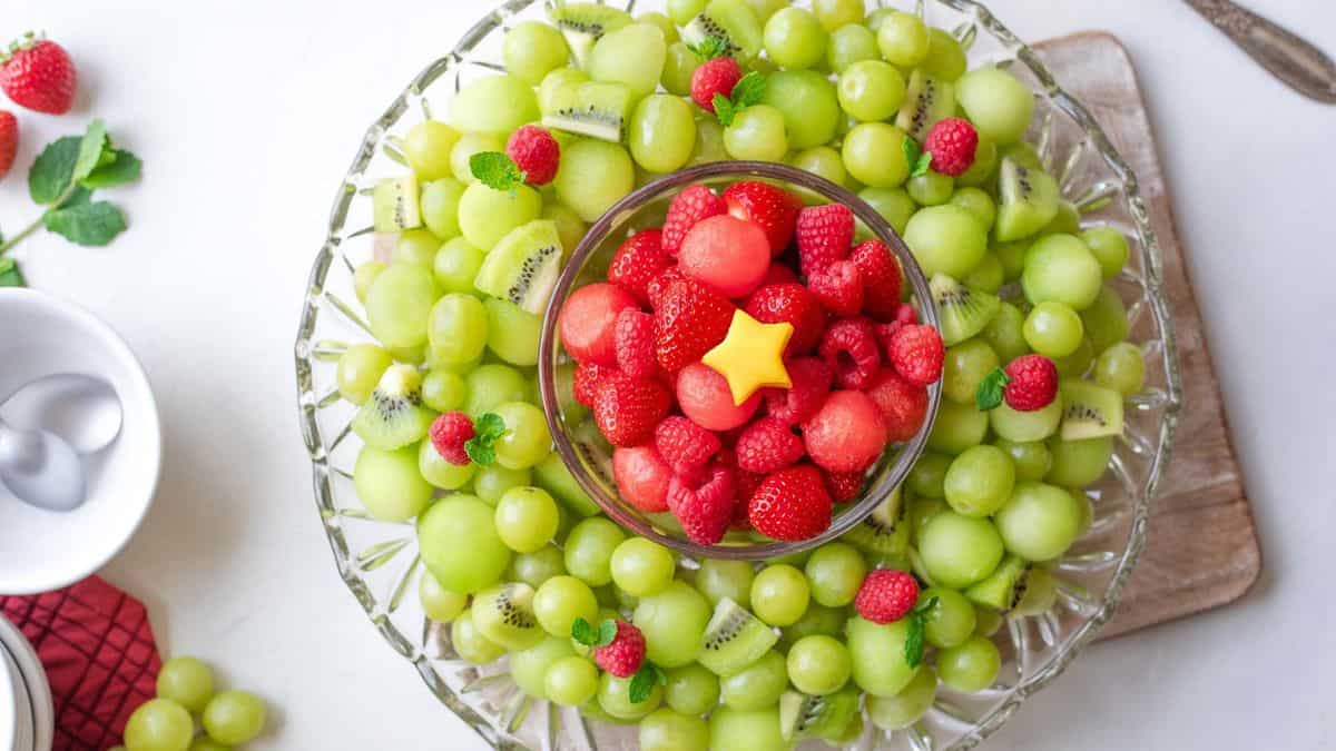 A clear glass platter filled with slices of kiwi and green grapes, and in the middle a smaller clear glass bowl with strawberries and watermelon. 