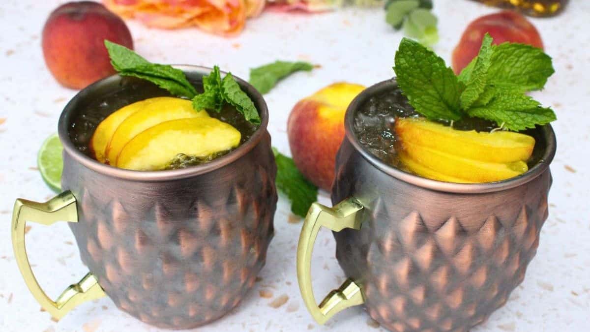 Two servings of Kentucky style Crown Peach Mule topped with slices of peaches and few mint leaves, 