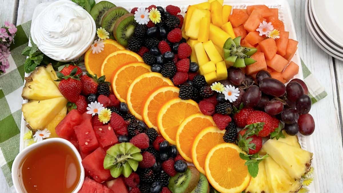 Fruit platter with cream and maple syrup dip and various fruits: slices of oranges, blueberries, blackberries, raspberries, kiwi, cantaloupes, mangoes, pineapples, grapes