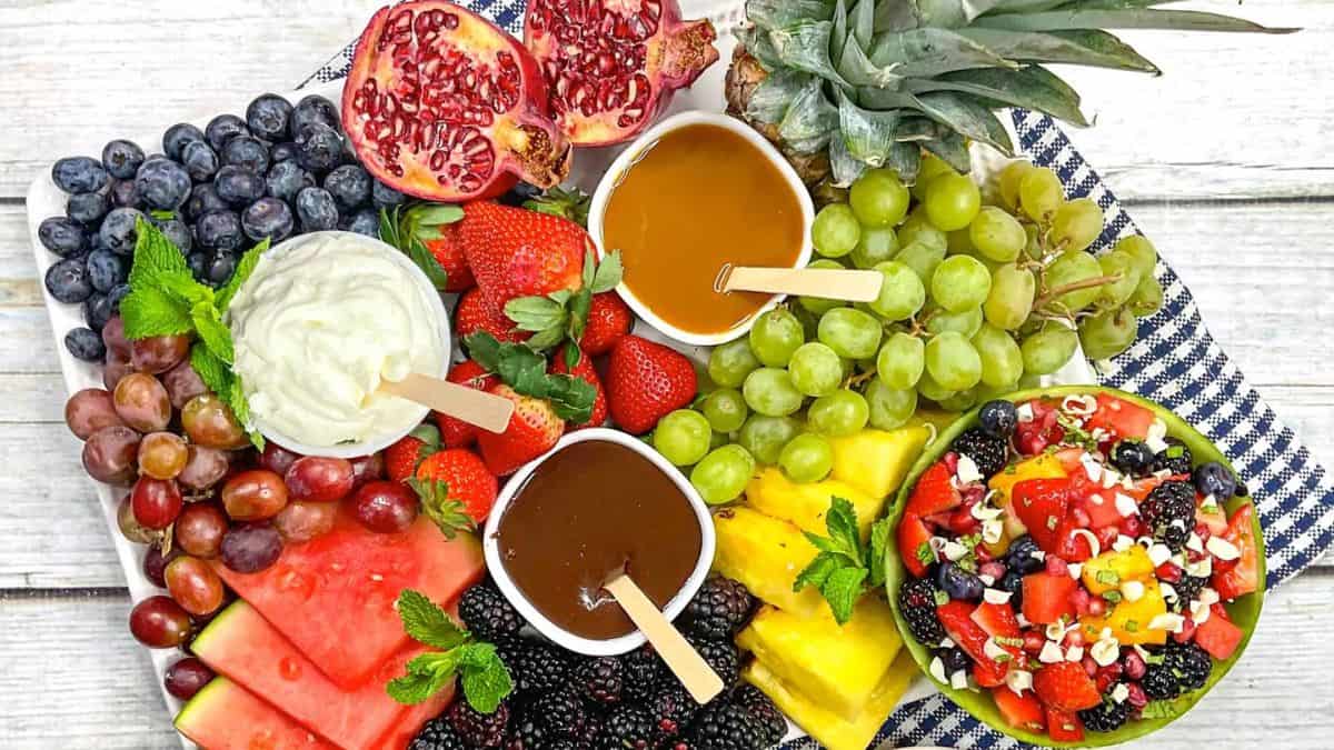 Fruit Charcuterie Board filled various fruits  and dips: pineapple, grapes, blueberries, strawberries, blackberries, watermelon, strawberries and a bowl of mixed fruits on the side. 