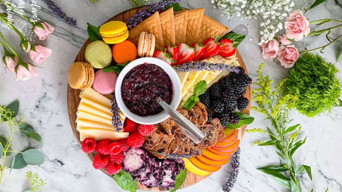 Fruit and dessert charcuterie board with raspberry jam filled with macarons, cheese slices, blackberries, raspberries, pastries, apples, strawberries