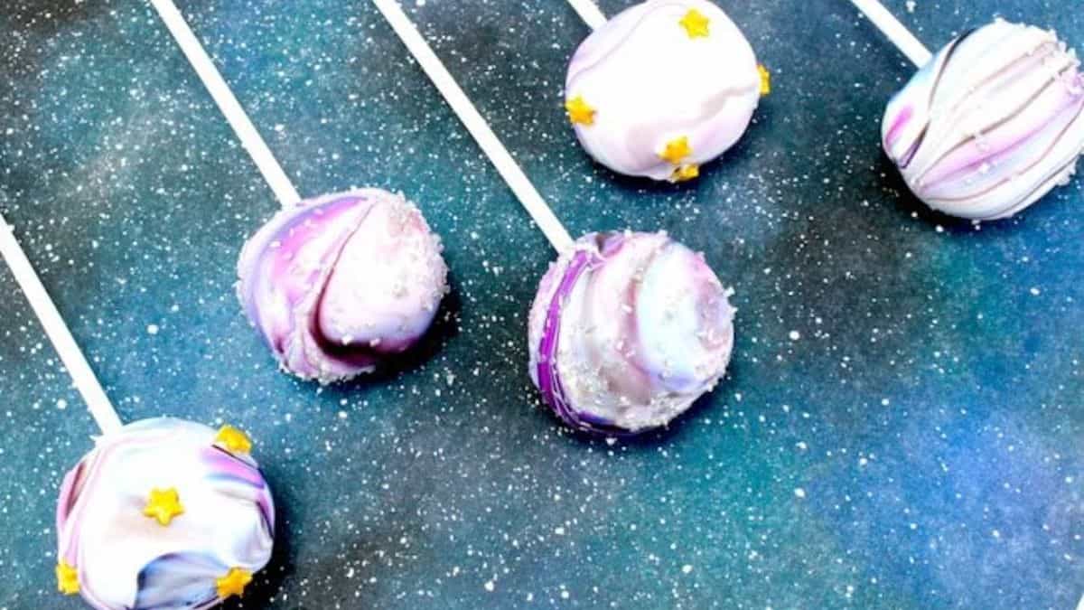A photo of five pieces of cake pops with galaxy design. 