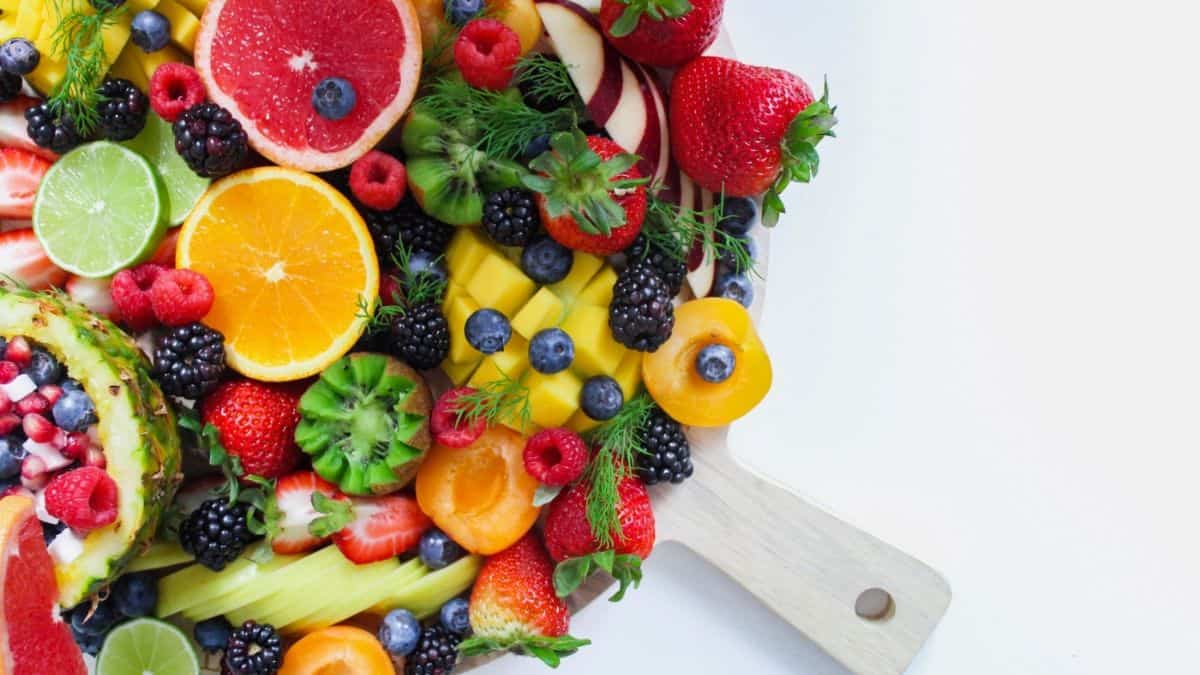 Fruit platter set on a round board: oranges, grapefruits, blueberries, blackberries, lime, pineapples, strawberries, mangoes, apples, raspberries, peaches.