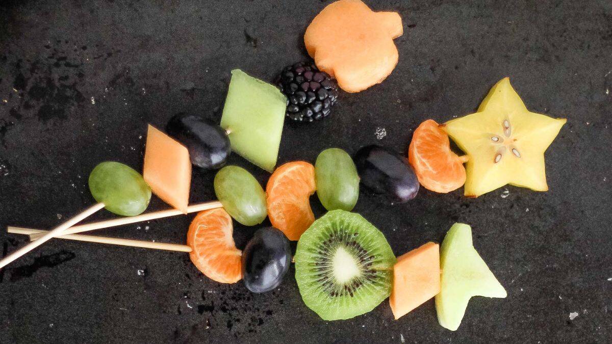 Three sticks of fruit kabobs that are Halloween themed with its shapes and color.