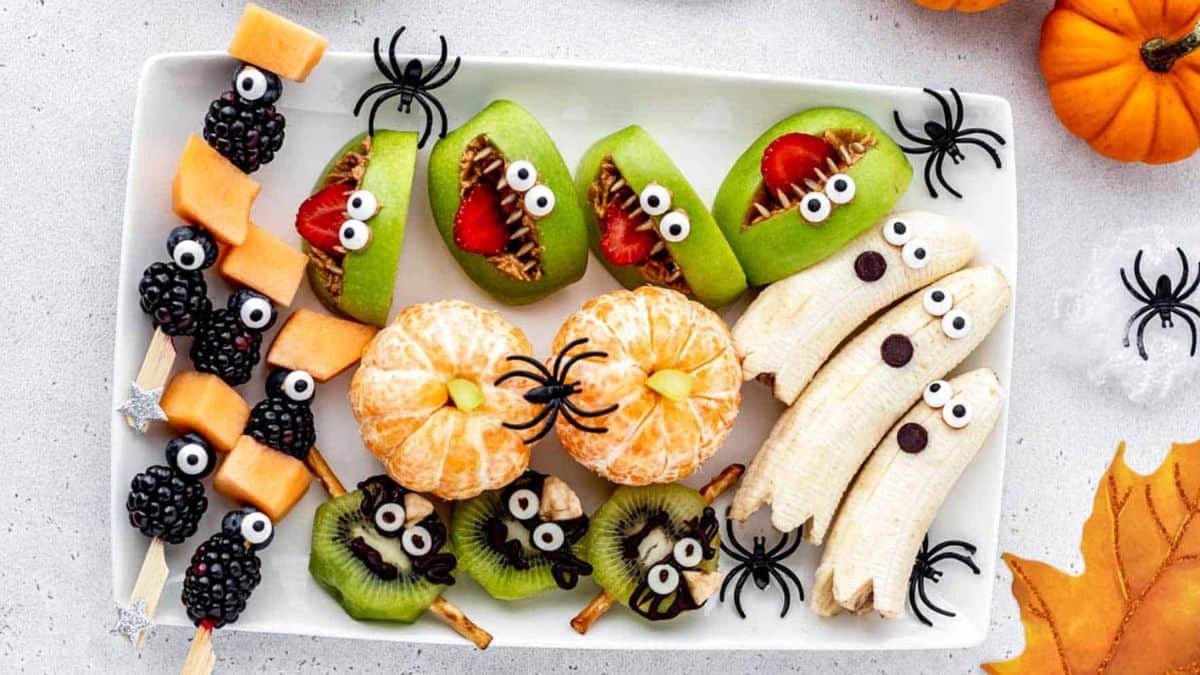 A platter of fruits designed for Halloween. Oranges, bananas, kiwis, apples, cantaloupe and blackberries. 