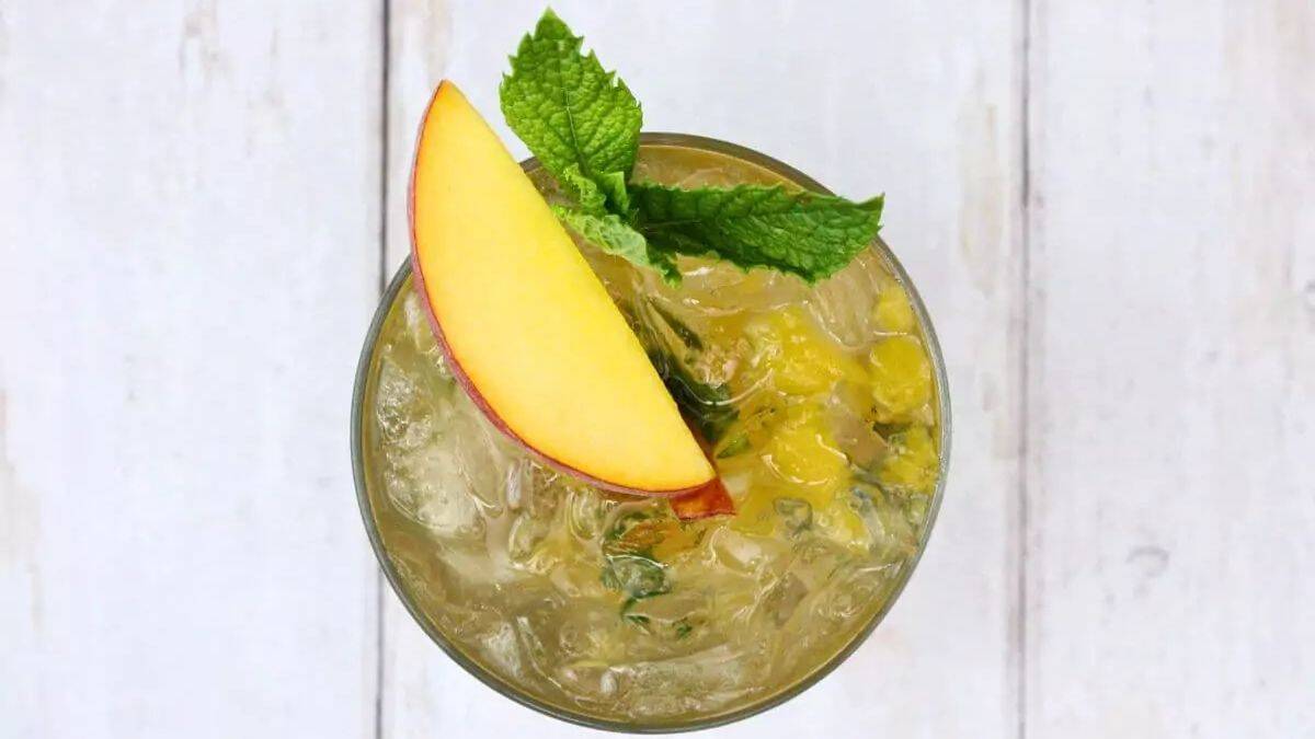 Top shot of a glass of Peach Mint Julep served with a slice of peach and a few pieces of mint leaves. 
