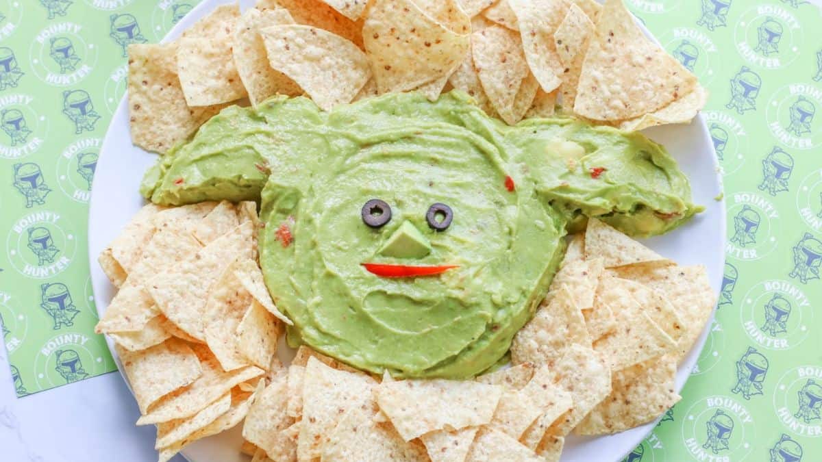 A plate filled with nachos and in the middle is a guacamole dipped shaped and designed as Yoda from Star Wars. 