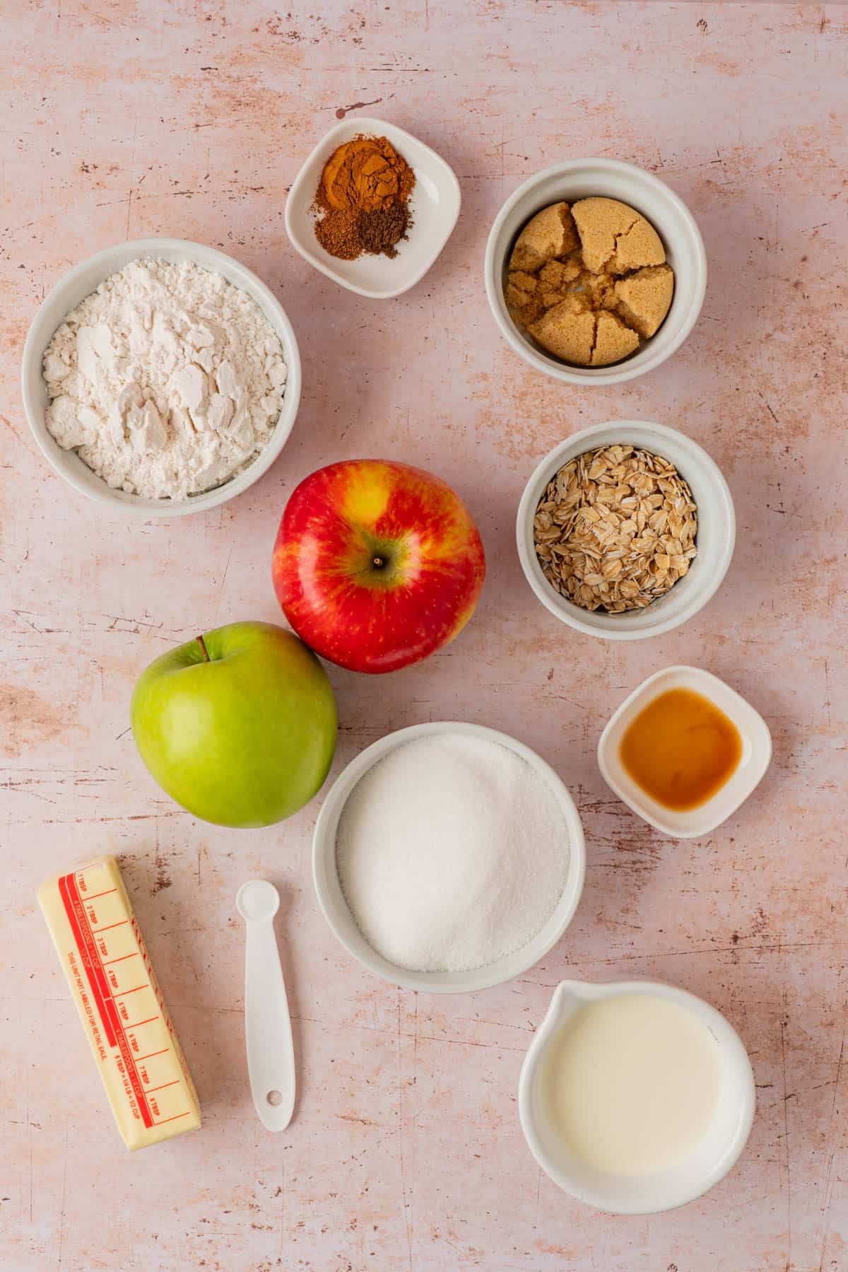 Overhead shot of ingredients for caramel apple pie bars, including flour, oats, brown sugar, cinnamon, granulated sugar, vanilla, butter, heavy cream, and red and green apples