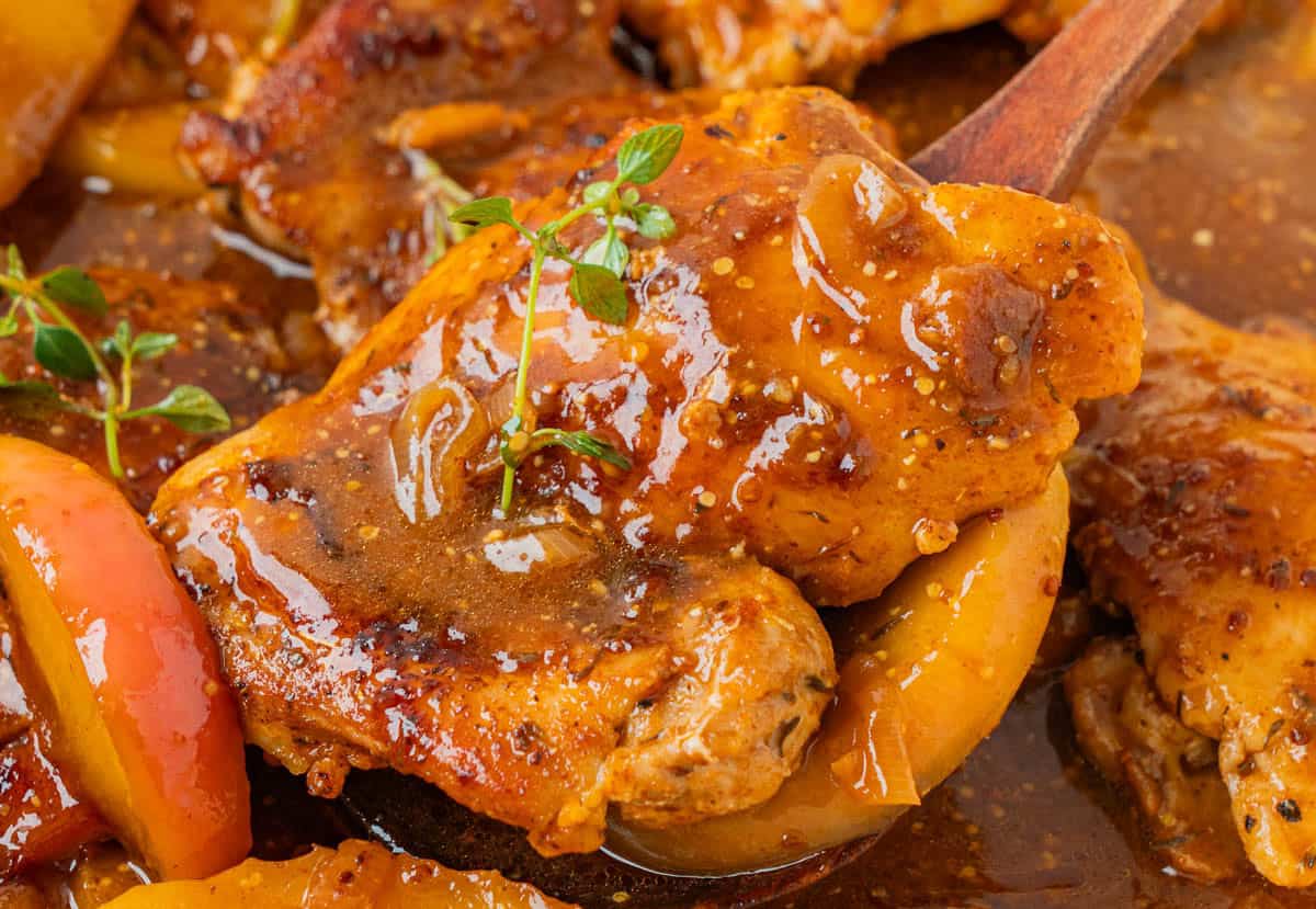 Close-up of a skillet apple cider chicken thigh coated in a glossy apple cider sauce with fresh thyme.