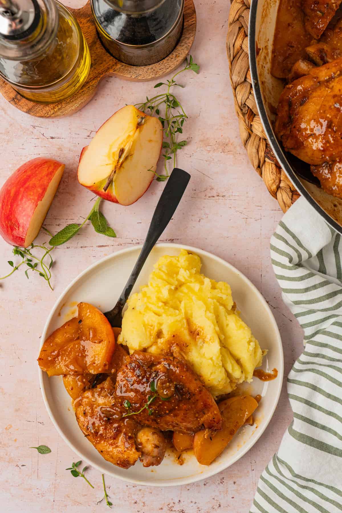 Overhead view of an apple cider chicken recipe served with mashed potatoes, apple wedges, and fresh herbs.
