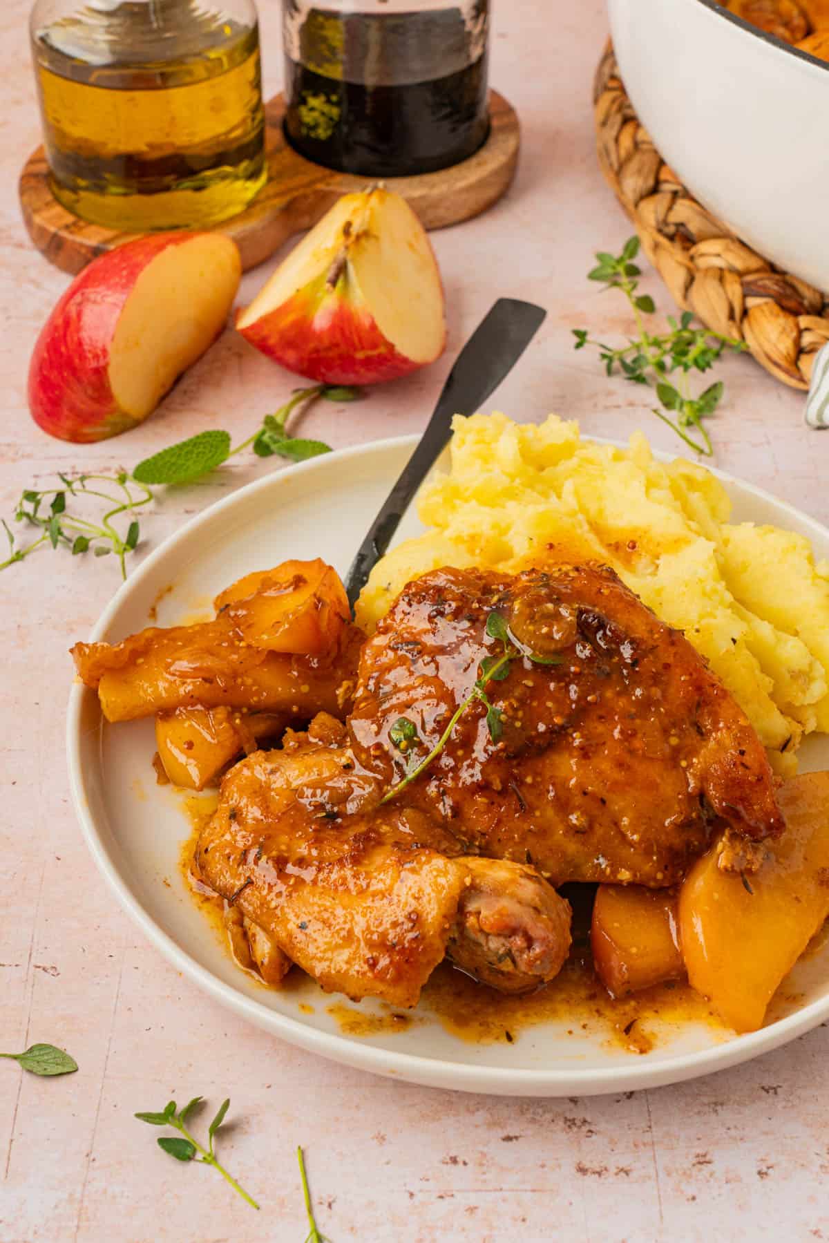 Apple cider chicken thigh served with creamy mashed potatoes and sautéed apples on a white plate.