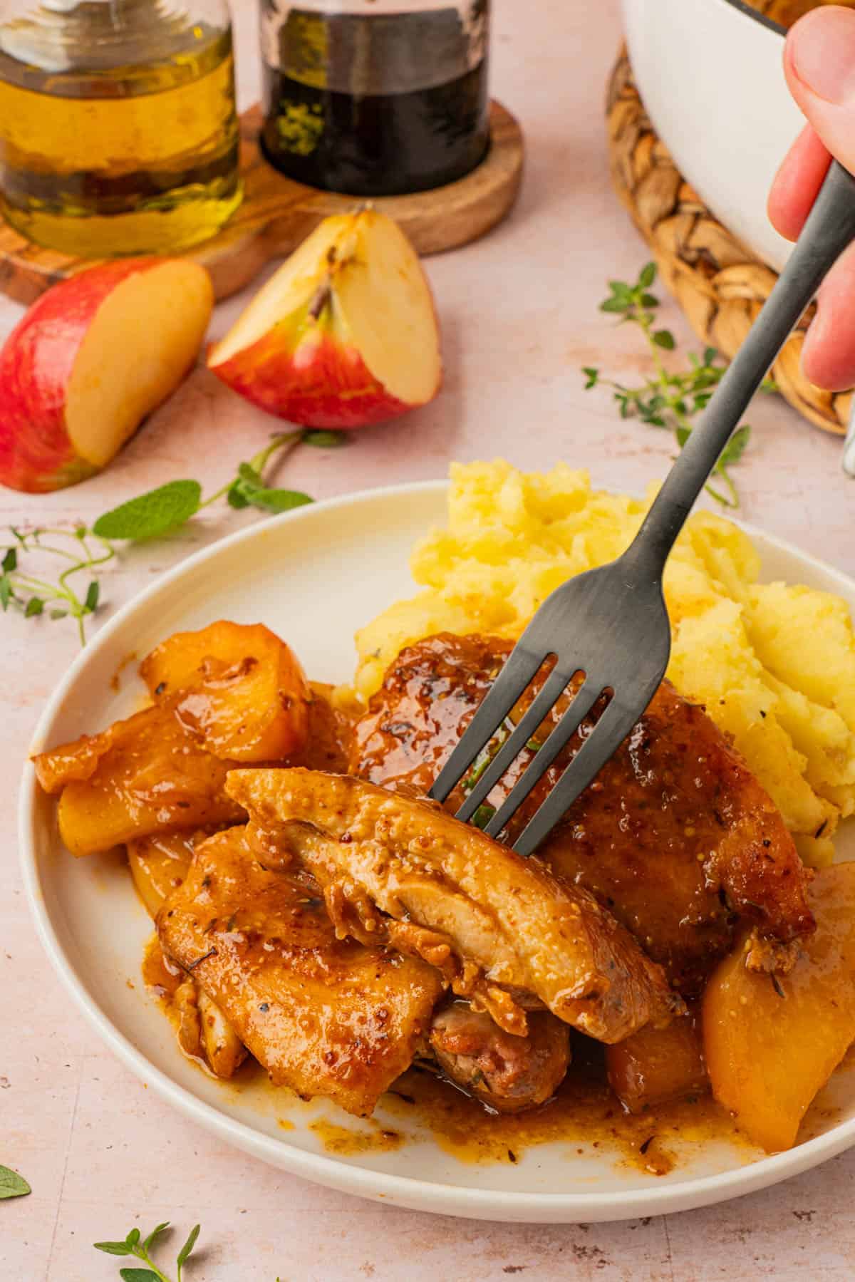 Fork cutting into a juicy chicken thigh in apple cider sauce, served with mashed potatoes.