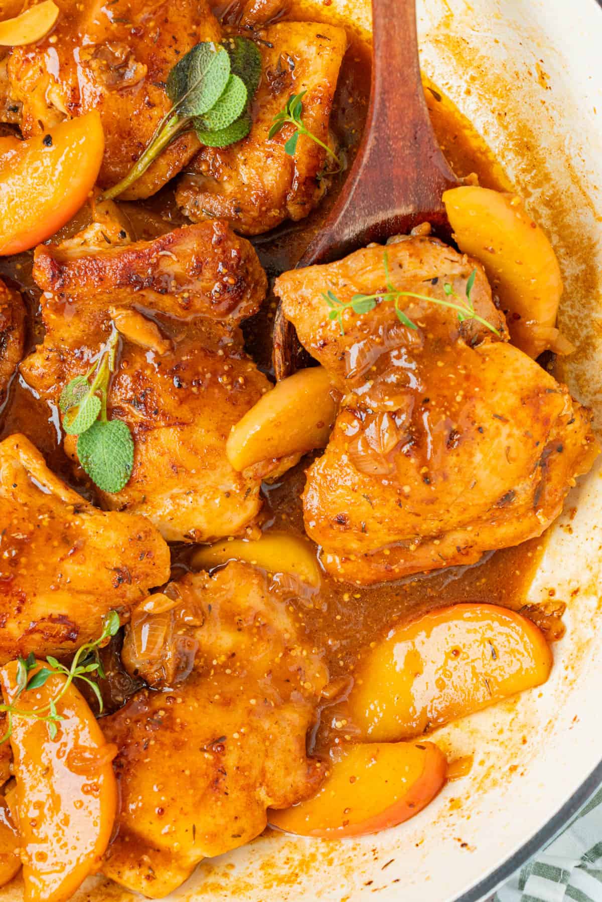 One skillet apple cider chicken thighs with sliced Honeycrisp apples, fresh sage, and thyme in a white pan.