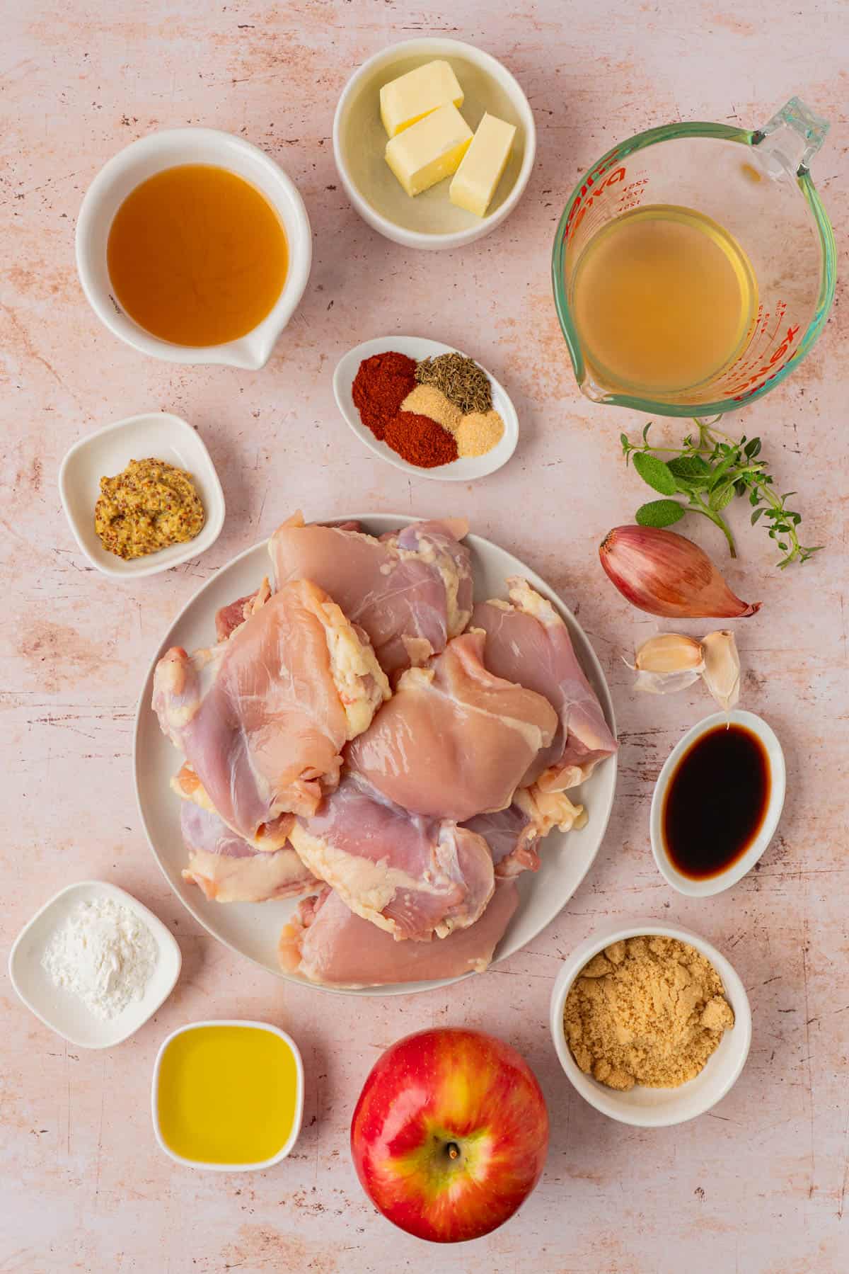 Ingredients for apple cider chicken, including chicken thighs, apple cider, Honeycrisp apple, shallot, garlic, and spices.