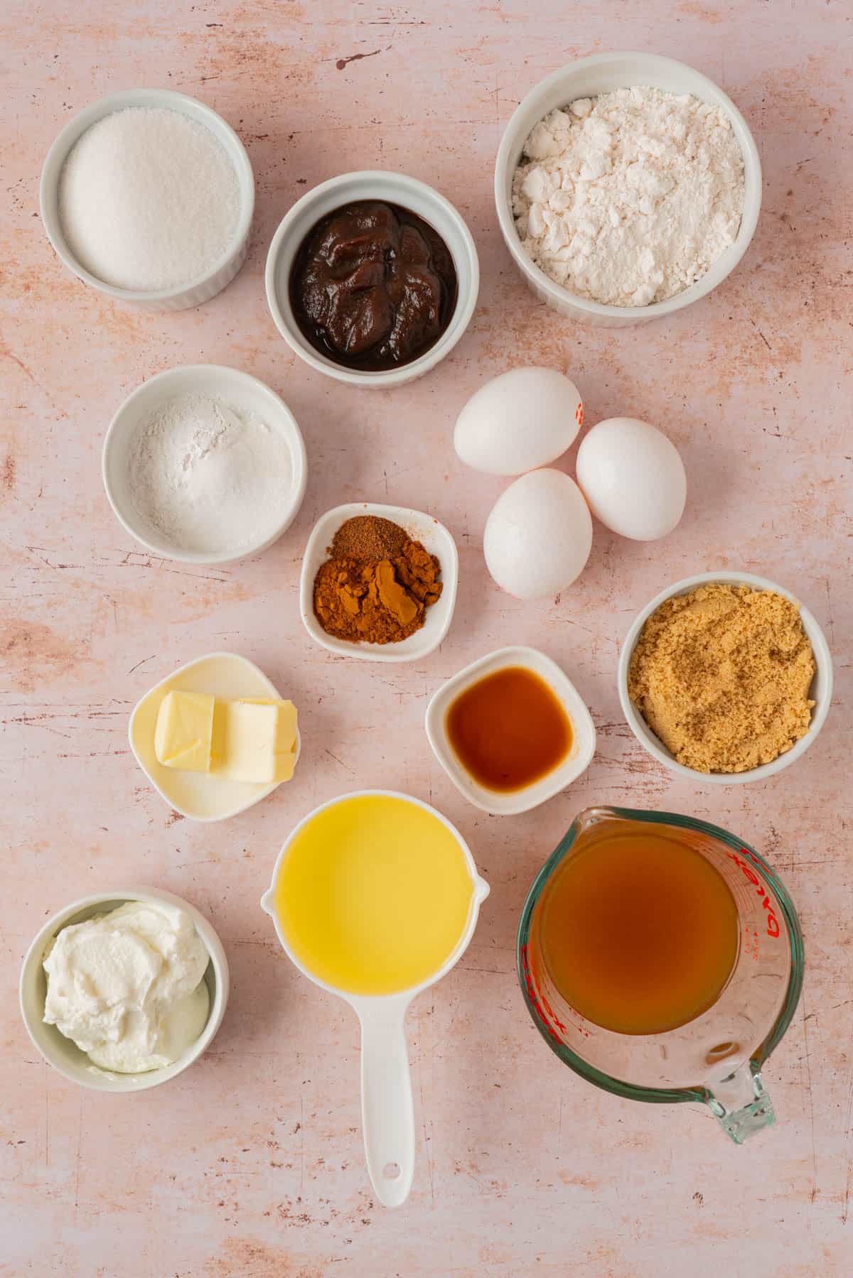 Ingredients for apple cider donut cake recipe, including apple cider, apple butter, flour, sugars, eggs, Greek yogurt, oil, butter, and spices