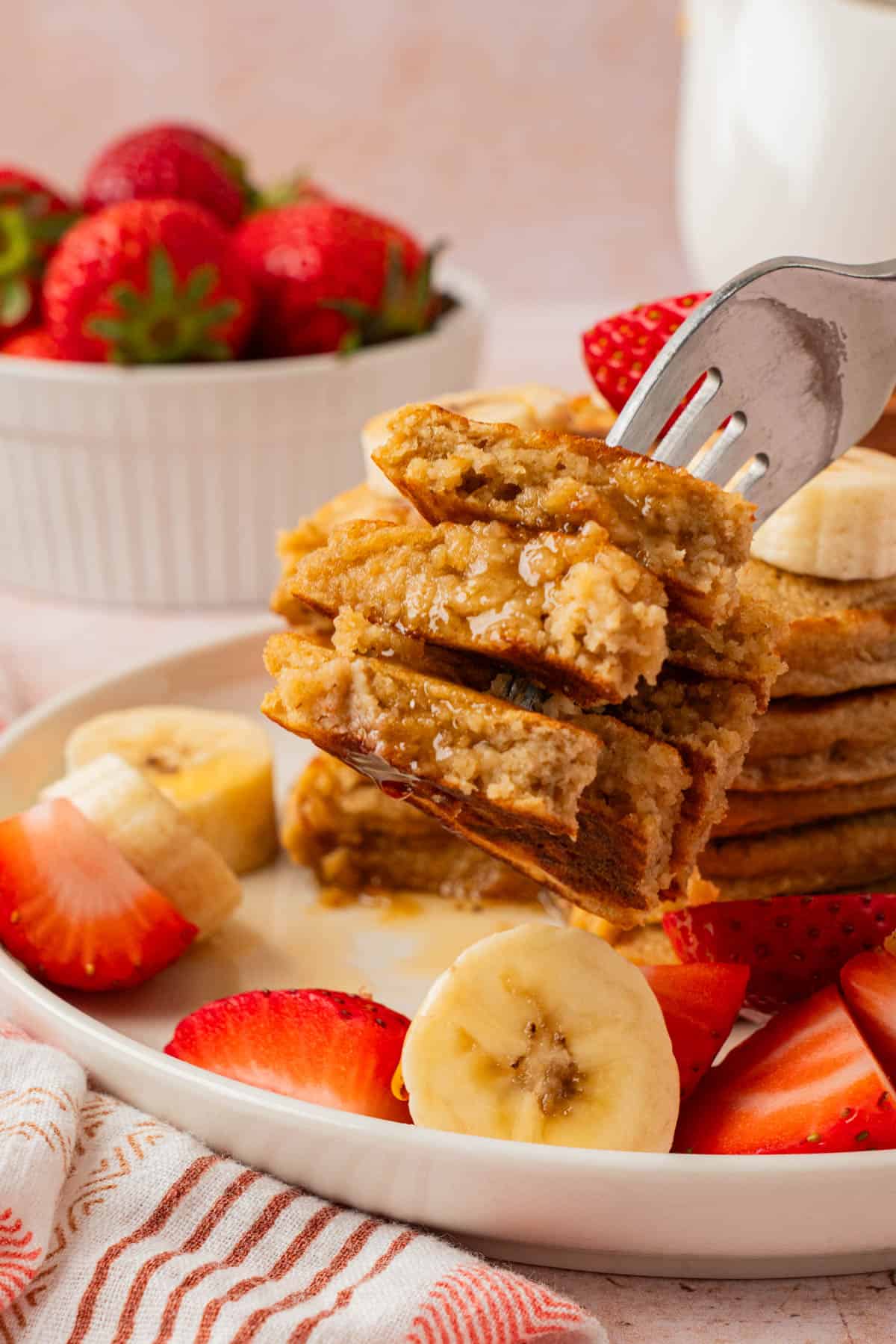 Close-up of a forkful of cottage cheese banana oatmeal pancakes drizzled with maple syrup, showing the moist oat texture.