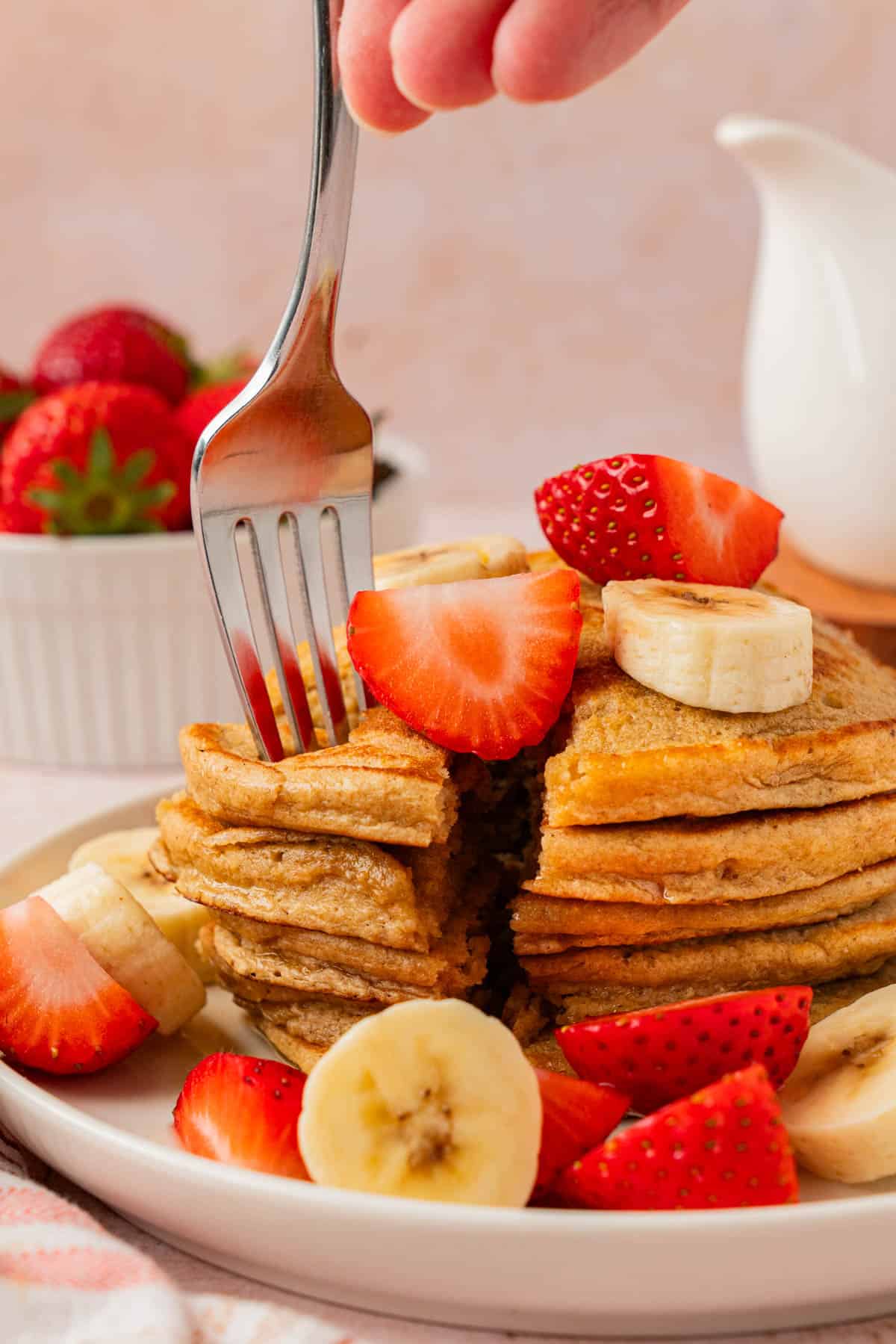 A fork cutting into a stack of healthy banana oat pancakes, showing the soft, tender layers inside.