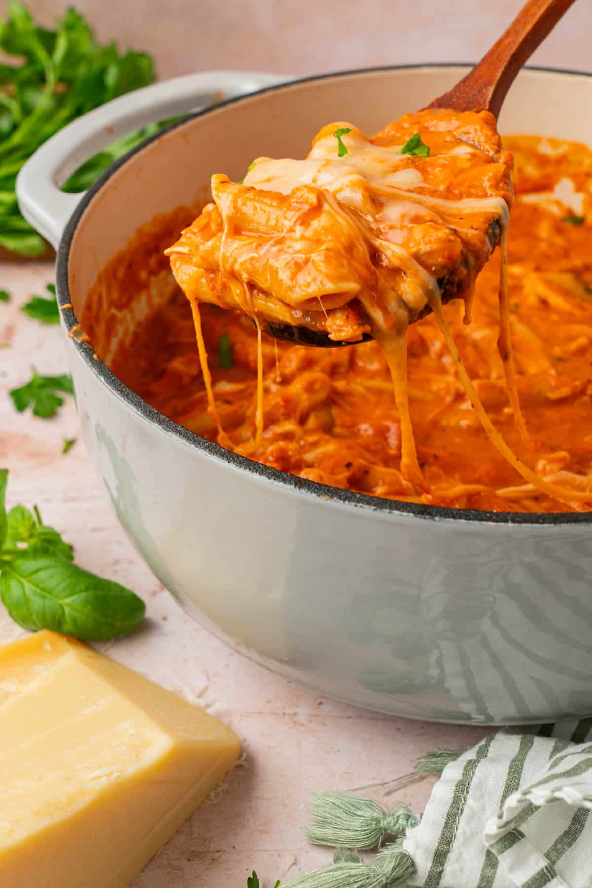 Cheesy chicken parmesan soup with a cheese pull on a wooden spoon over a pot of soup
