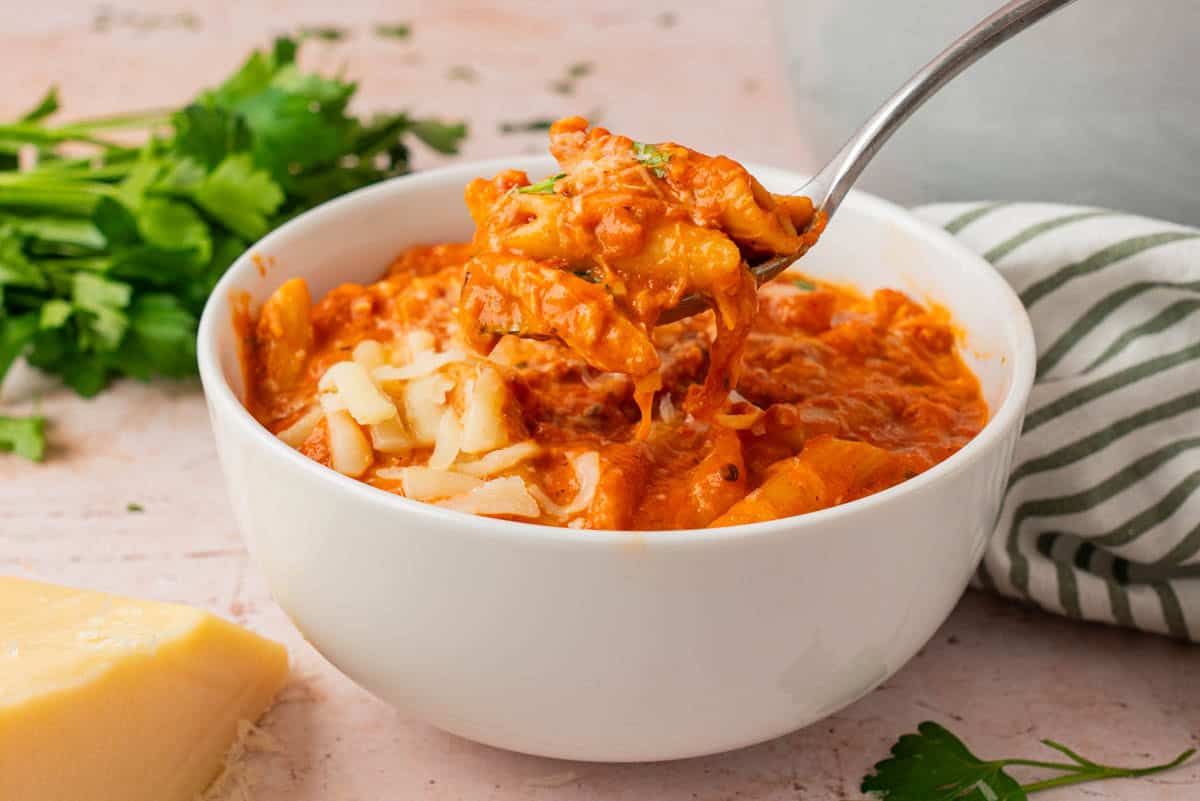 Spoonful of creamy parmesan chicken soup with tender penne and melted cheese above a white bowl