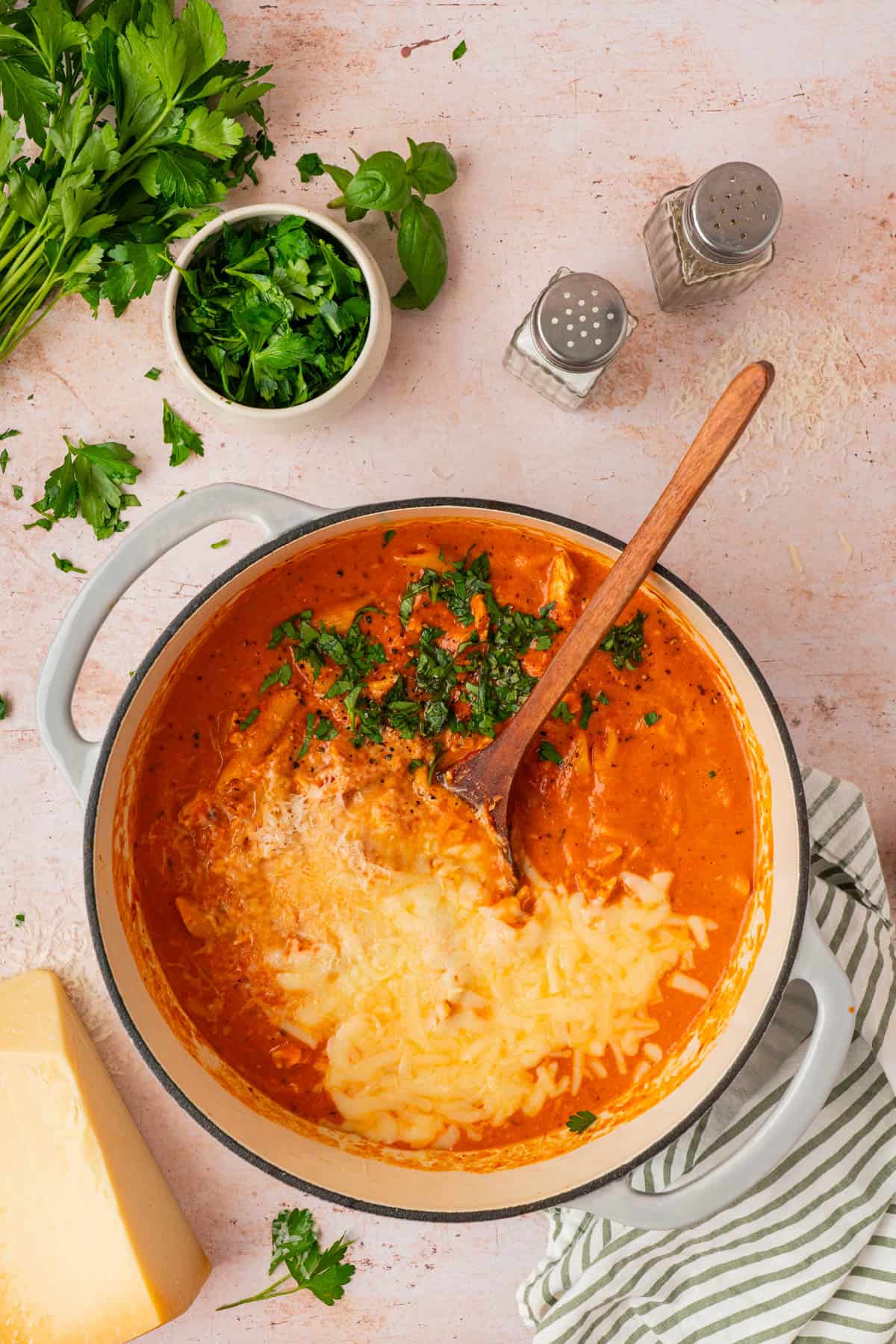 Creamy chicken parmesan soup in a Dutch oven topped with melted mozzarella, parmesan, and fresh herbs
