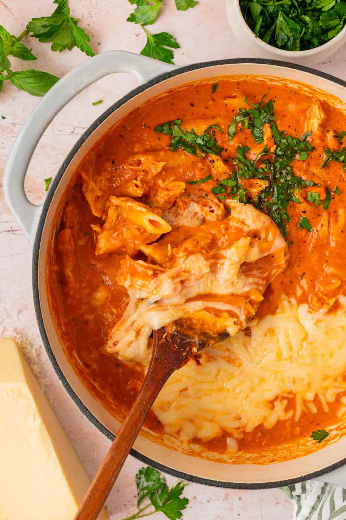 Easy chicken parmesan soup with penne, shredded chicken, and gooey melted cheese on a wooden spoon
