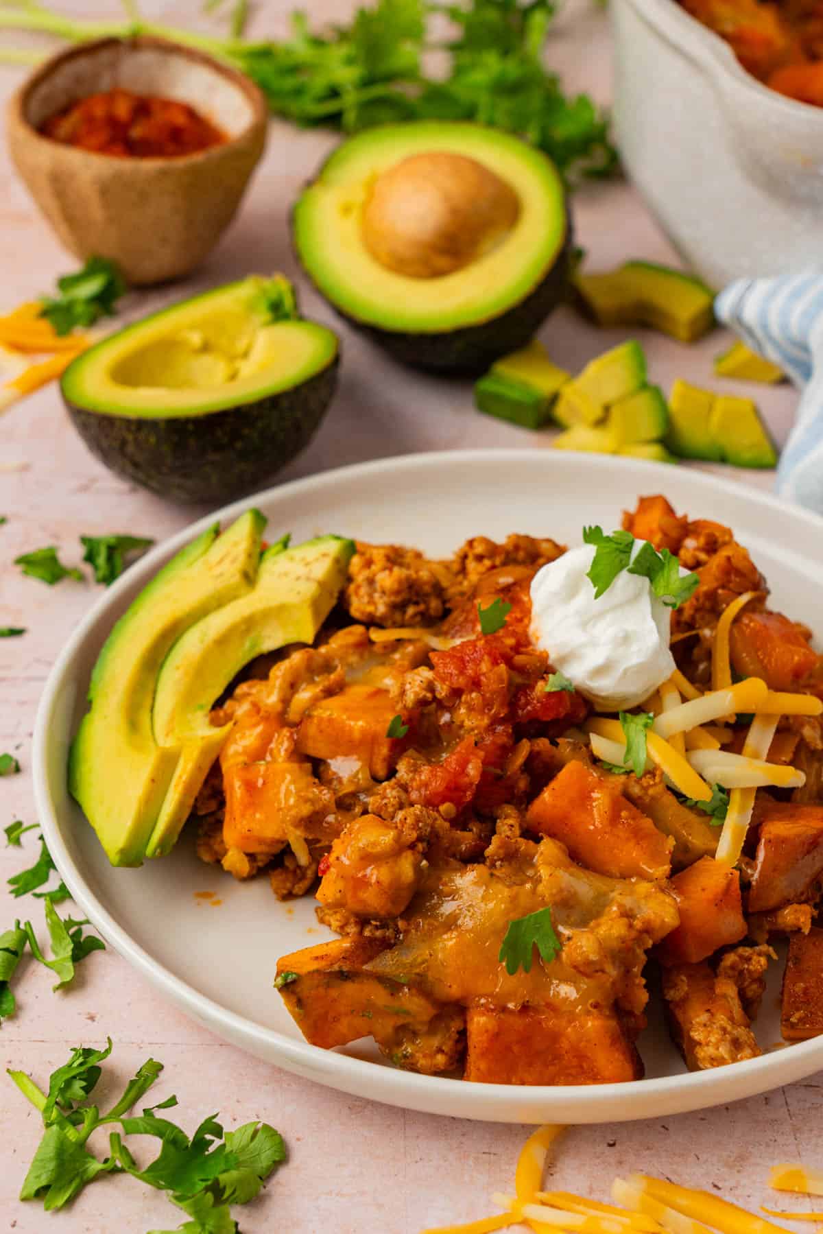 Plate of ground turkey sweet potato skillet delight topped with Greek yogurt, shredded cheese, salsa, and avocado slices.