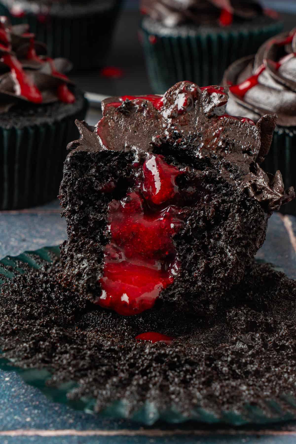 A black velvet cupcake for Halloween cut open to show the red raspberry "blood" filling inside.