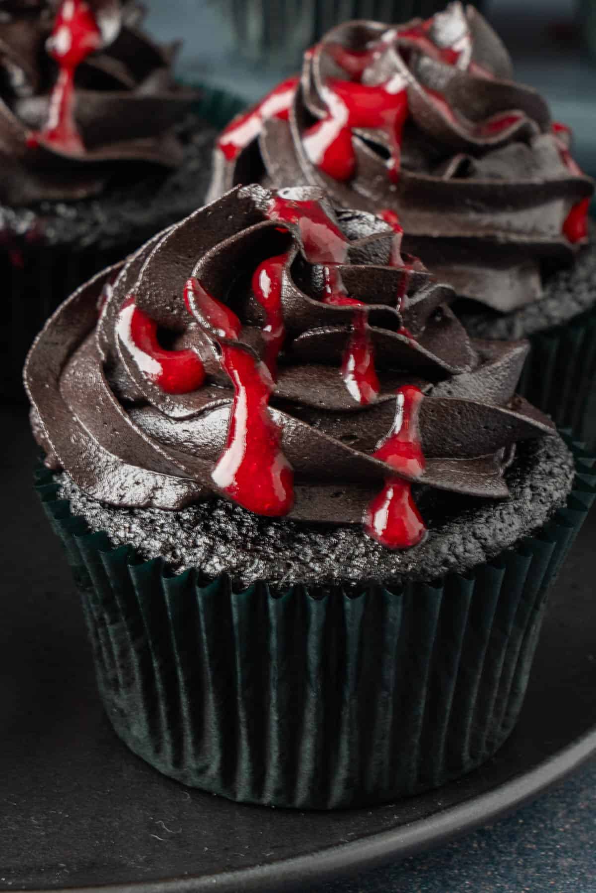 Close-up of Halloween-themed cupcakes with black frosting and a dripping raspberry drizzle, a spooky cupcake decoration idea.