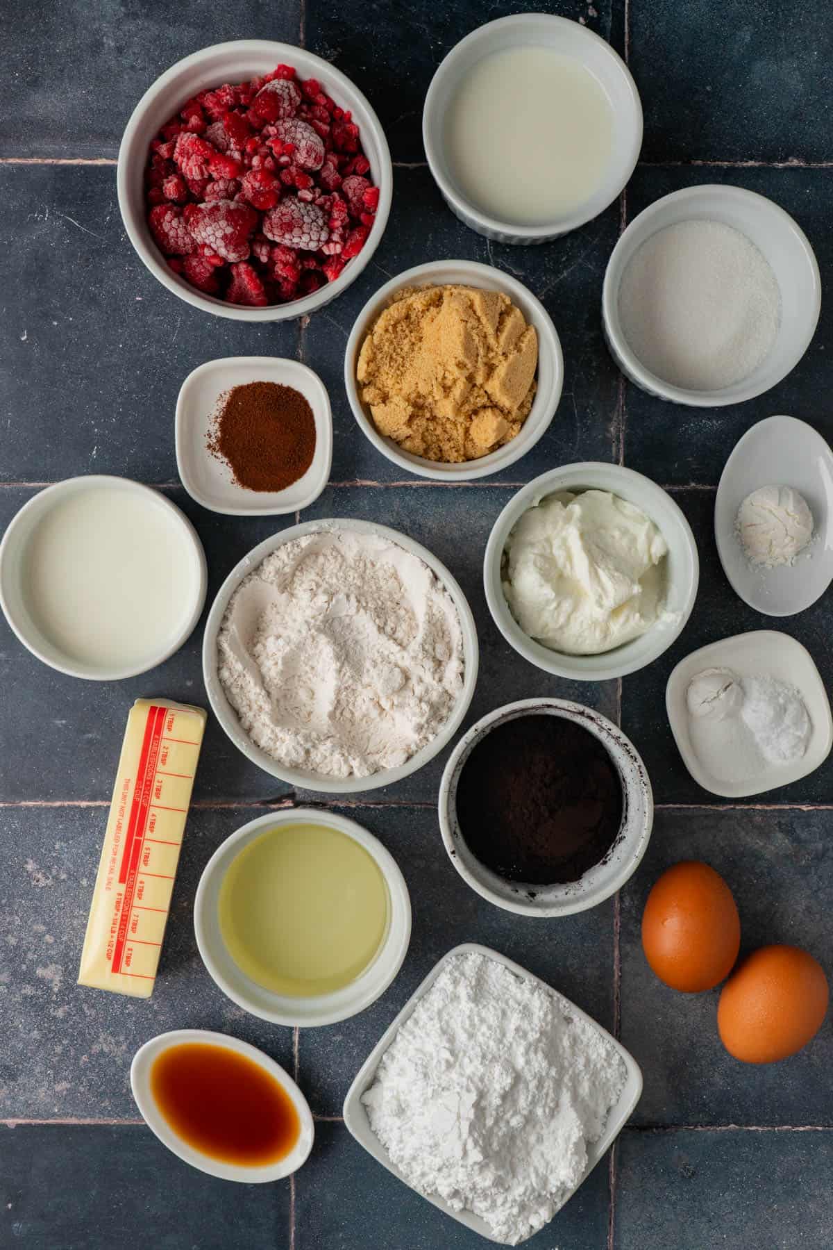 Ingredients for black cocoa cupcakes, including black cocoa powder, frozen raspberries, flour, sugars, Greek yogurt, butter, and eggs.