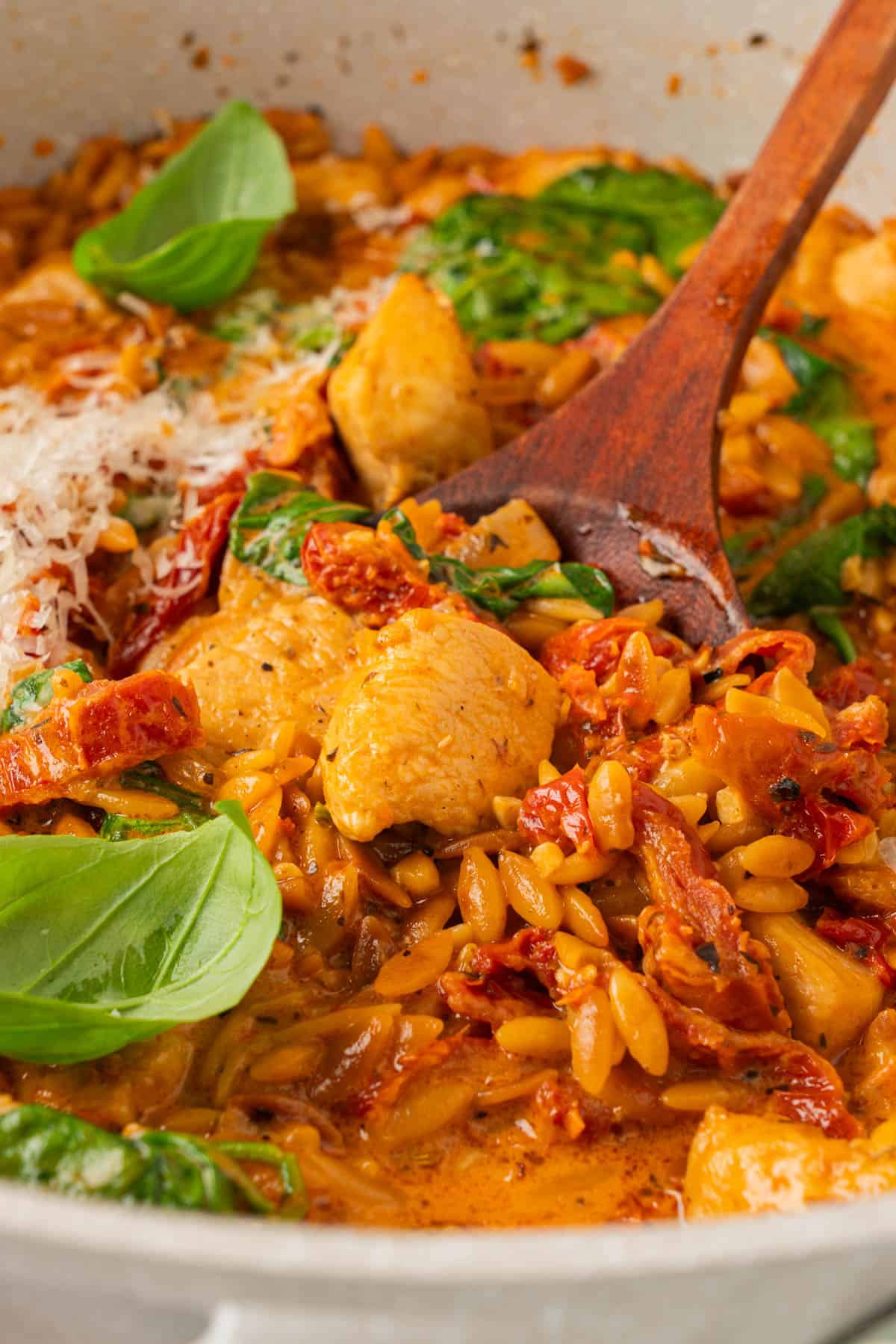 Close-up of a marry me chicken and orzo skillet showing chicken pieces, toasted orzo, sun-dried tomatoes, and wilted spinach.