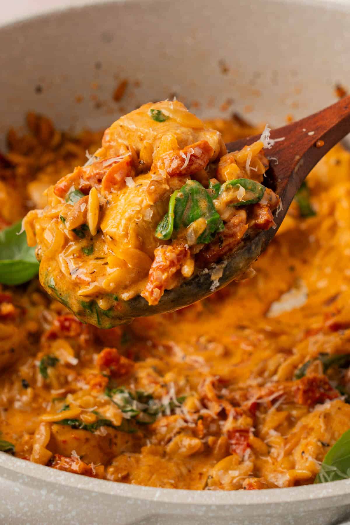 Wooden spoon lifting creamy marry me chicken and orzo with tender chicken, spinach, and sun-dried tomatoes from the skillet.