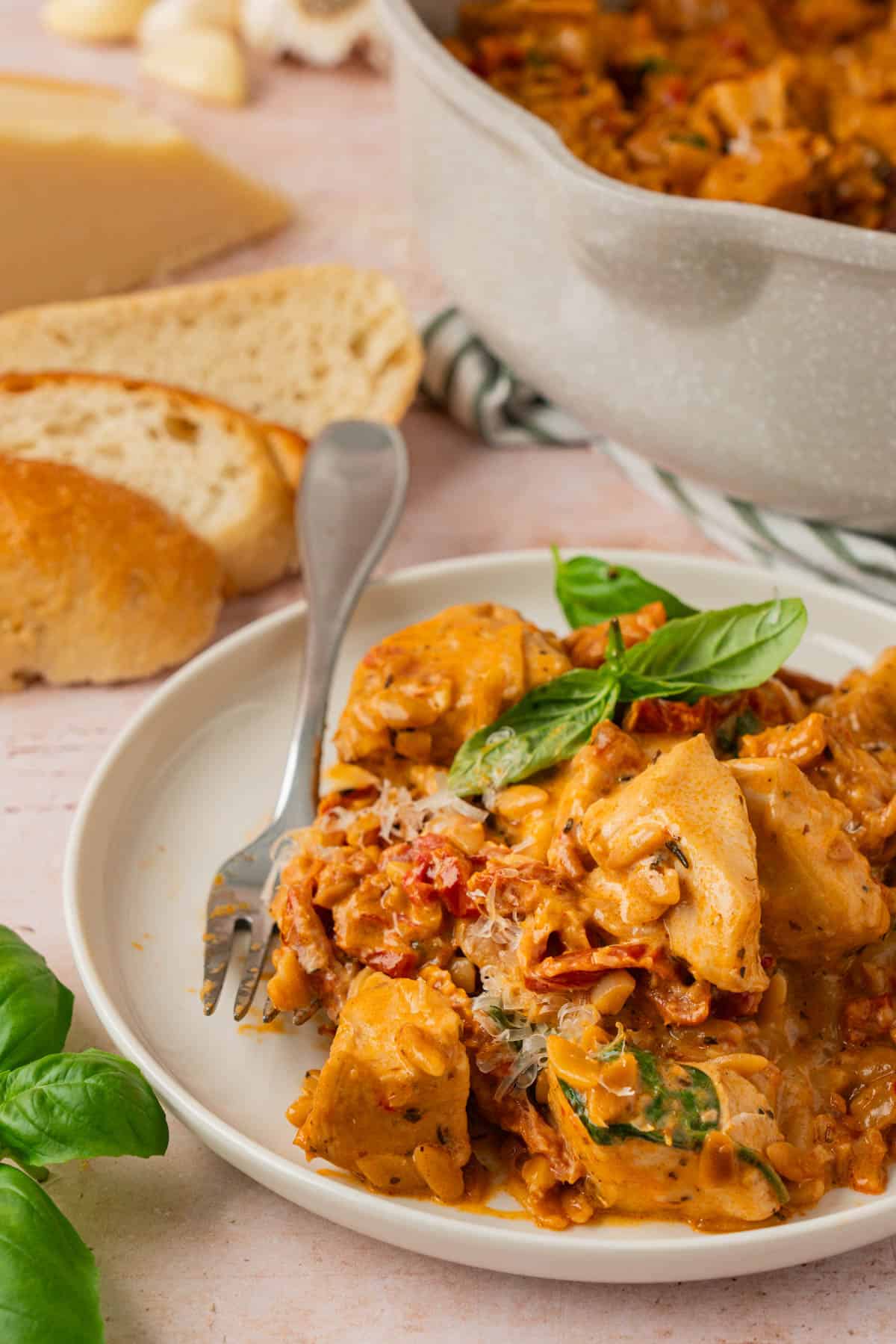 Easy chicken orzo recipe served on a white plate with fresh basil, a fork, and sliced crusty bread on the side.