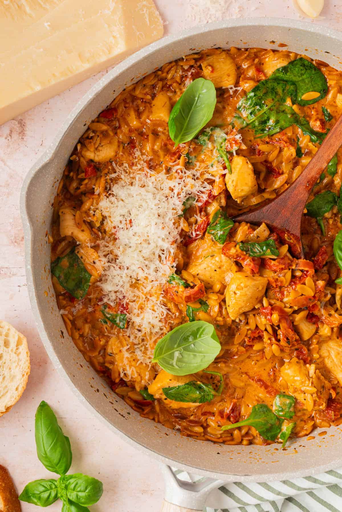 One pan marry me chicken orzo topped with grated parmesan, fresh basil, spinach, and sun-dried tomatoes in a white skillet.