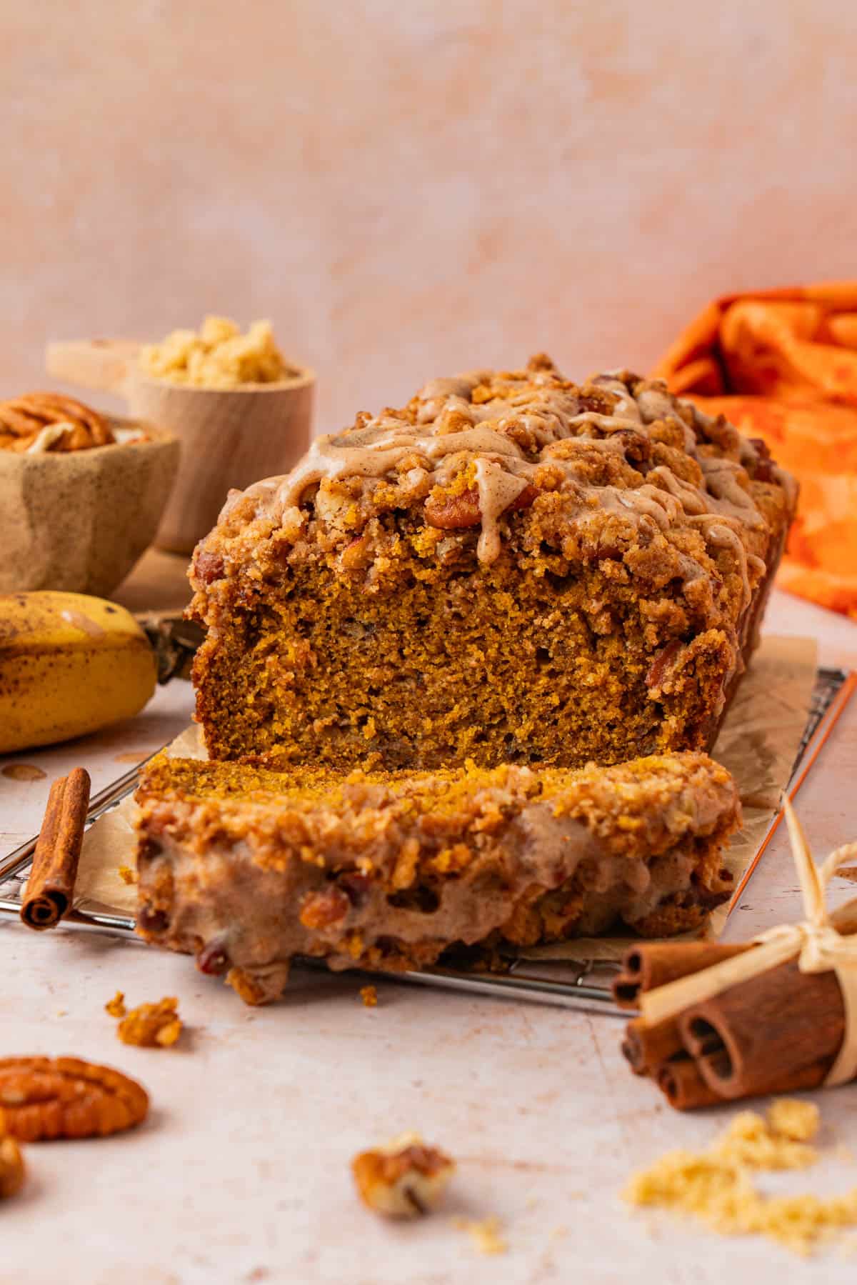 Close-up side view of pumpkin banana bread loaf with pecan streusel and cinnamon glaze, sliced open to show the moist orange crumb