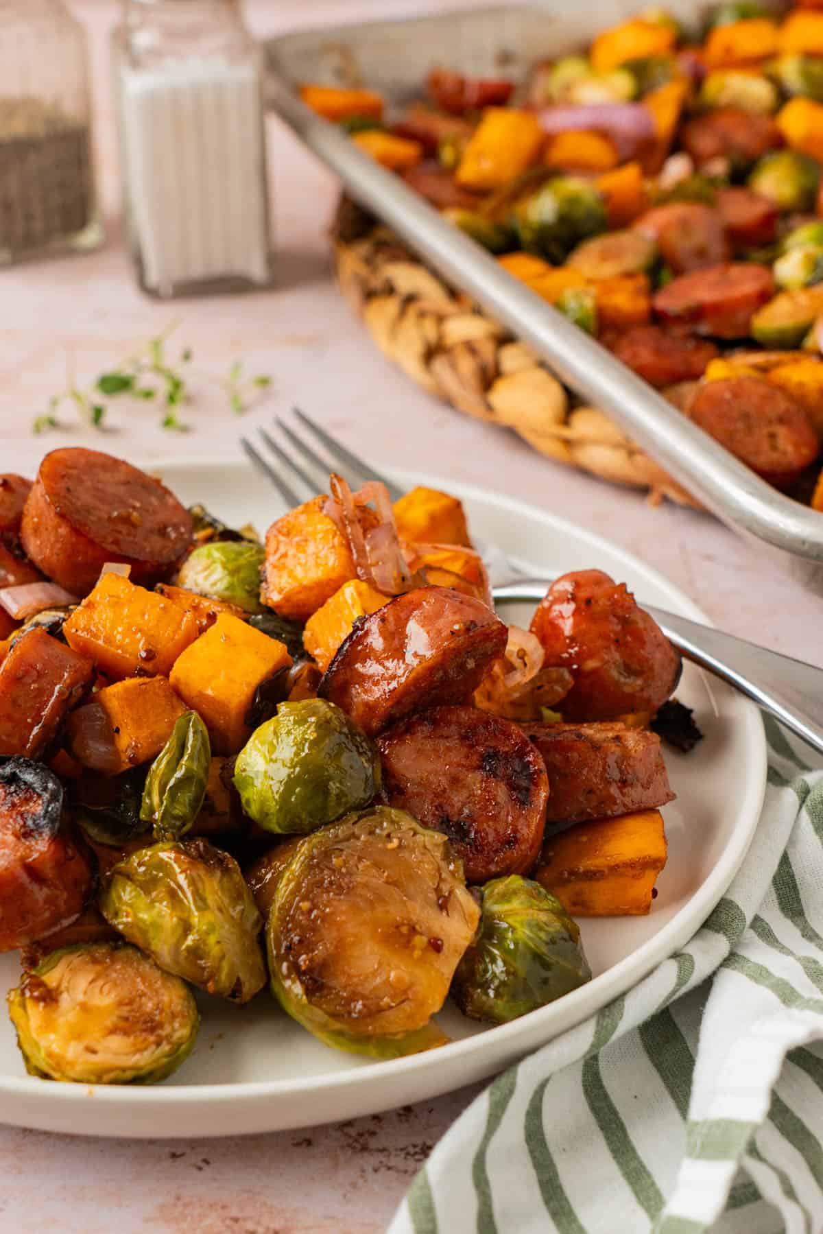 Plate of sheet pan chicken sausage & veggies with a fork, with the roasted sheet pan in the background.