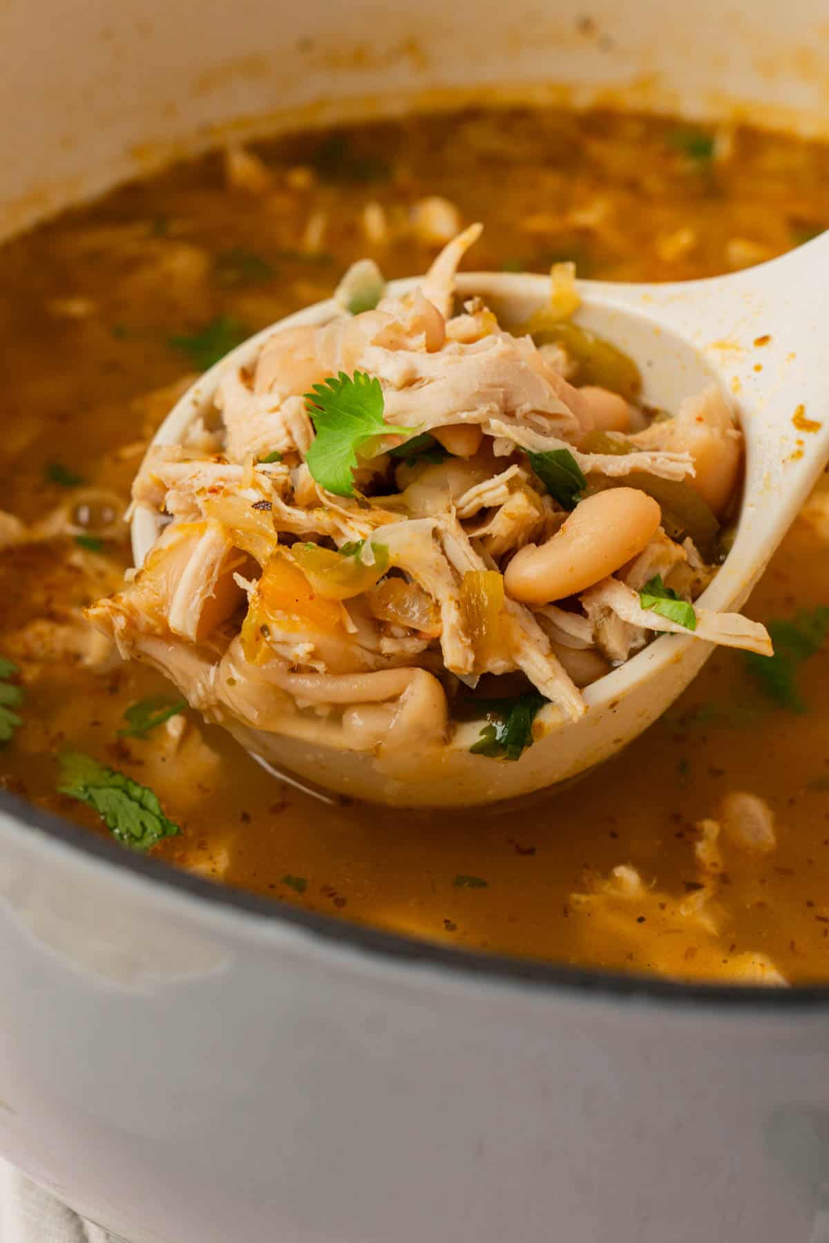 Ladle lifting shredded chicken and white beans out of the chili pot