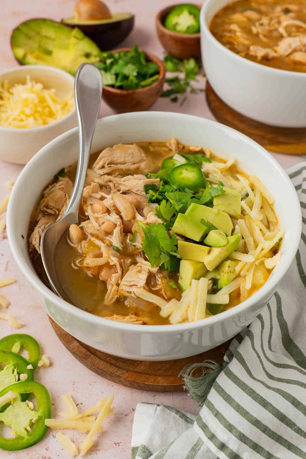 White bean chicken chili in a bowl garnished with cheese, avocado and jalapeño