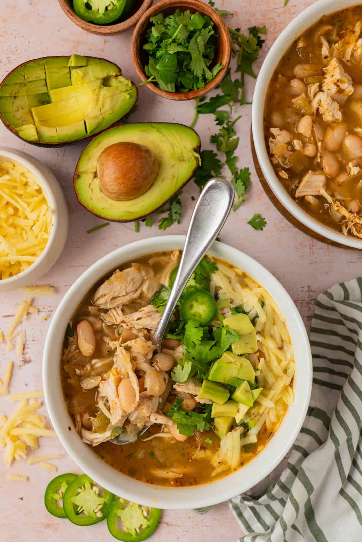 Overhead shot of white bean chicken chili garnished with avocado, cheese, cilantro and jalapeño