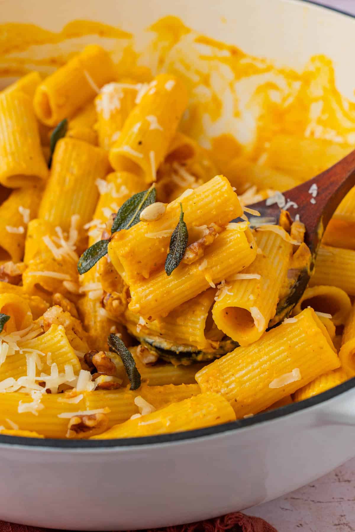 Wooden spoon lifting rigatoni coated in creamy pumpkin pasta sauce with crispy sage and walnuts.