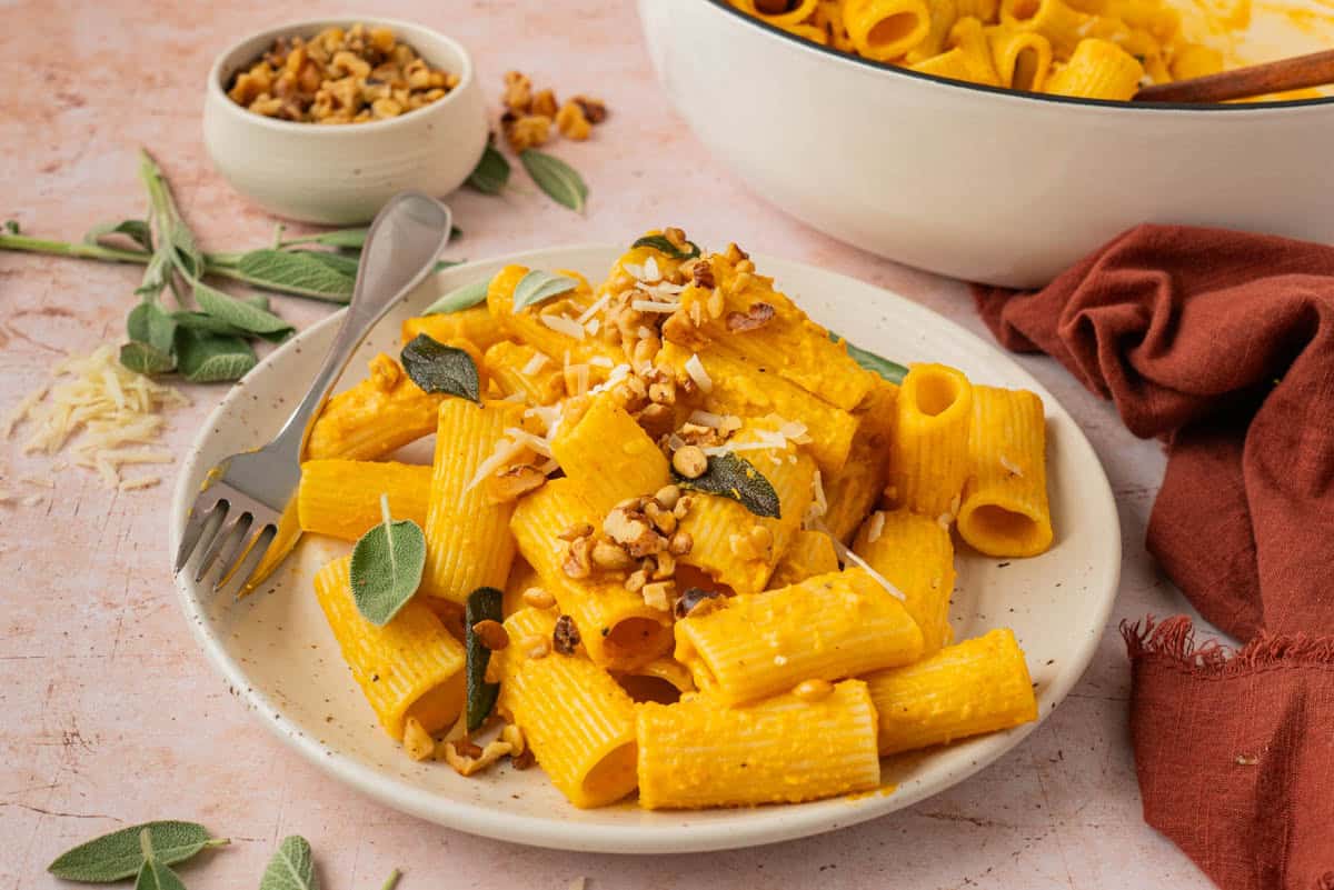 Serving of fall pumpkin pasta with sage and toasted walnuts on a speckled plate with a fork.