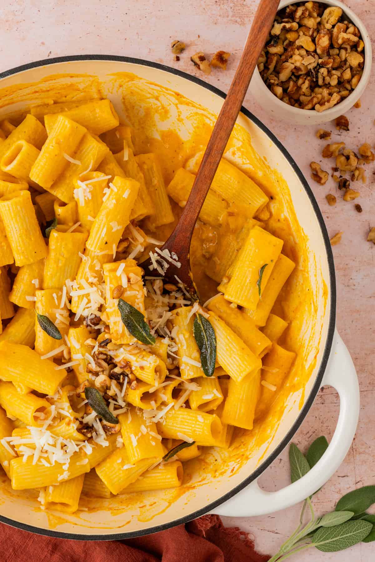 Creamy pumpkin pasta with sage in a white skillet, topped with Gruyere, crispy sage, and toasted walnuts.
