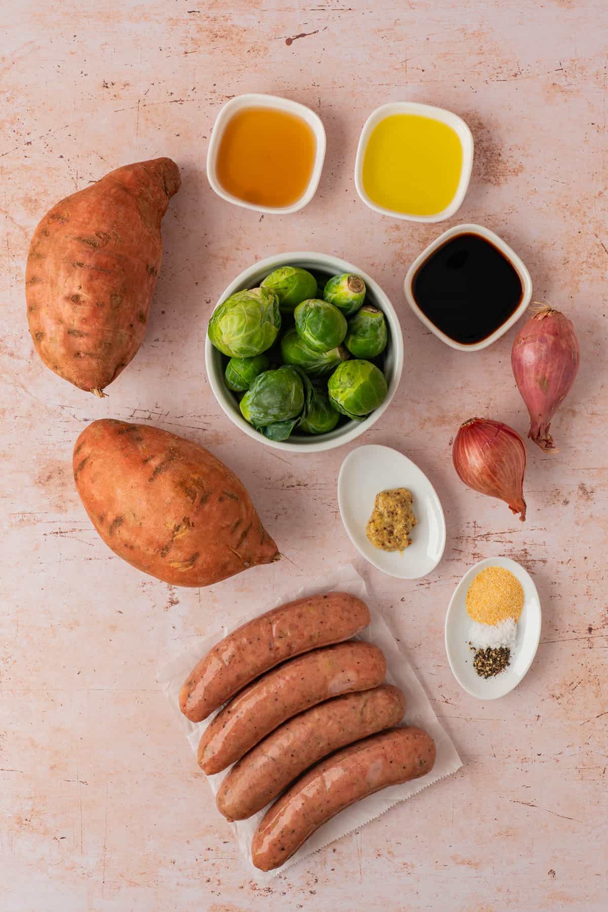 Ingredients for sheet pan chicken sausage: sweet potatoes, Brussels sprouts, shallots, chicken sausage, maple syrup, olive oil, and balsamic vinegar.