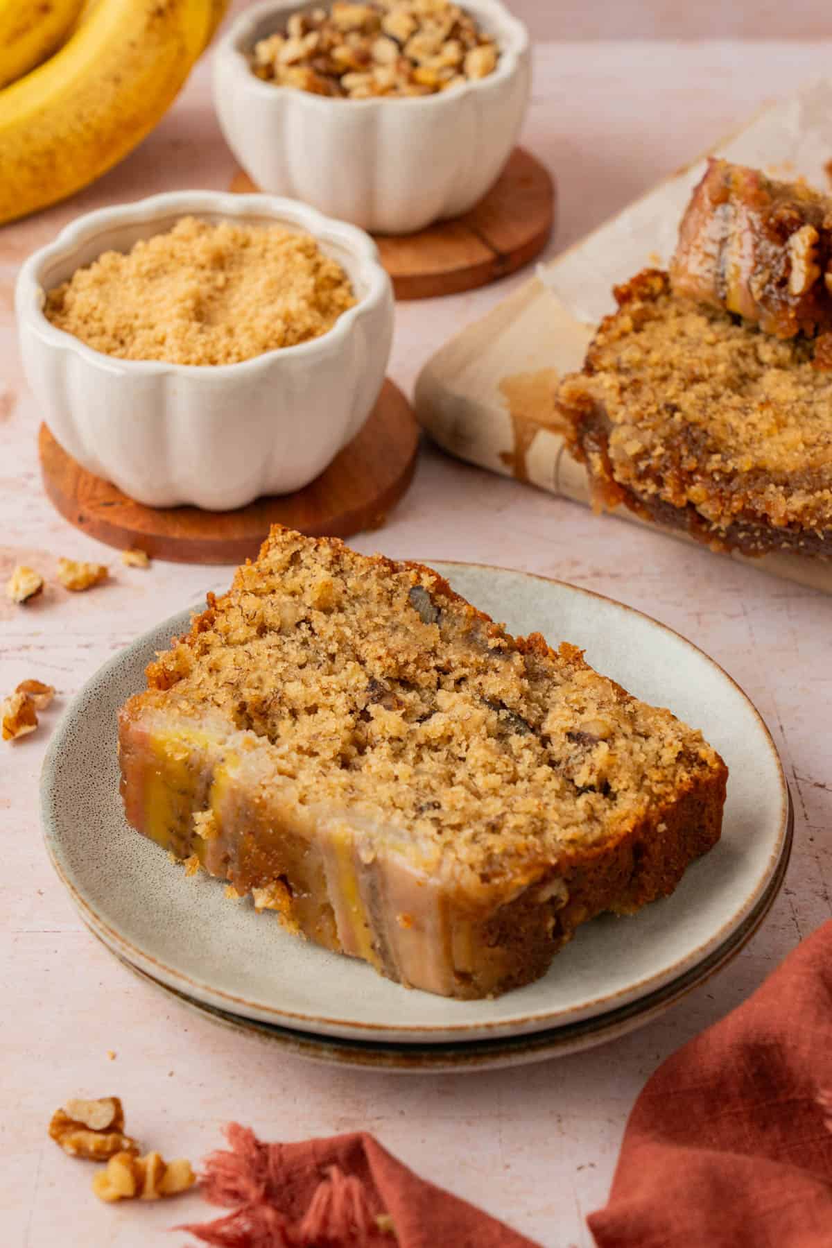 A slice of the best caramel banana bread on a plate with bowls of brown sugar and walnuts