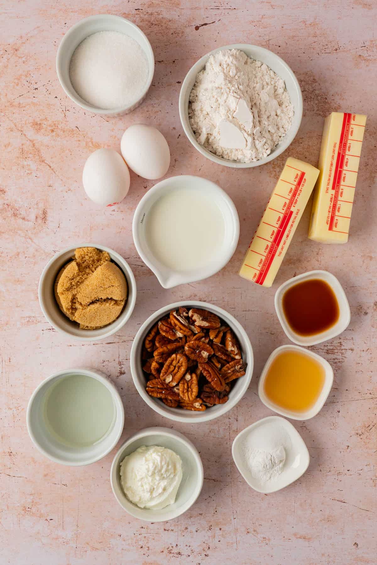 Ingredients for an upside down pecan cake recipe, including pecans, butter, brown sugar, flour, eggs, milk, Greek yogurt, corn syrup, vanilla, and bourbon.